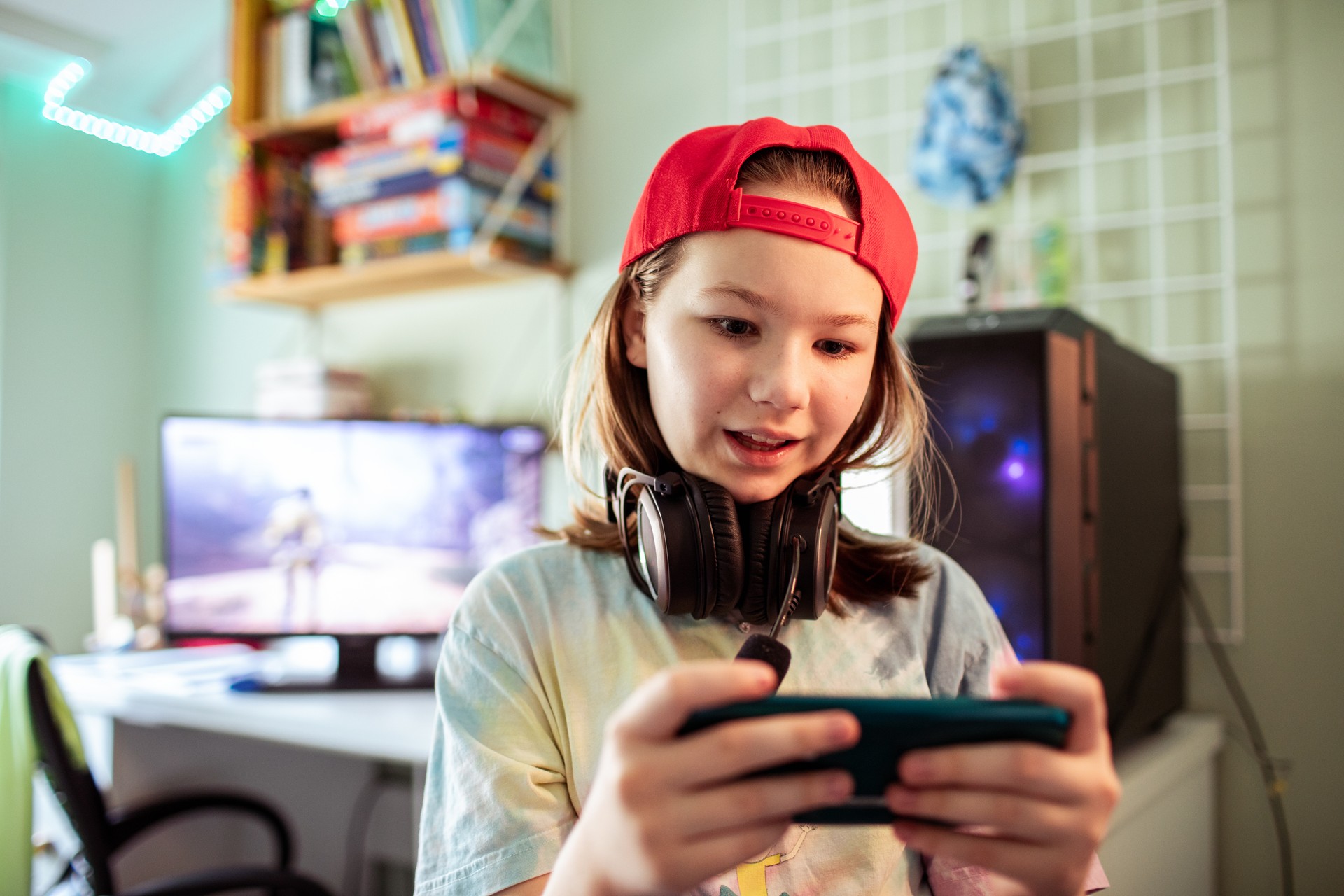 Young girl playing games on her smart phone in her bedroom by the desktop computer